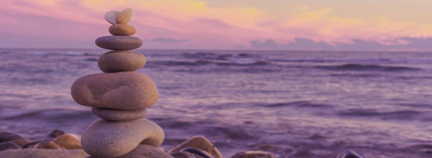 a stack of rocks balanced against an ocean at sunset - representing balanced not busy